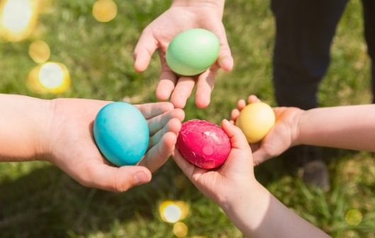 Four children&#039;s hands shown above a grassy area each holding a painted Easter egg