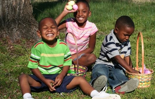 Three children sat on the grass holding Easter eggs