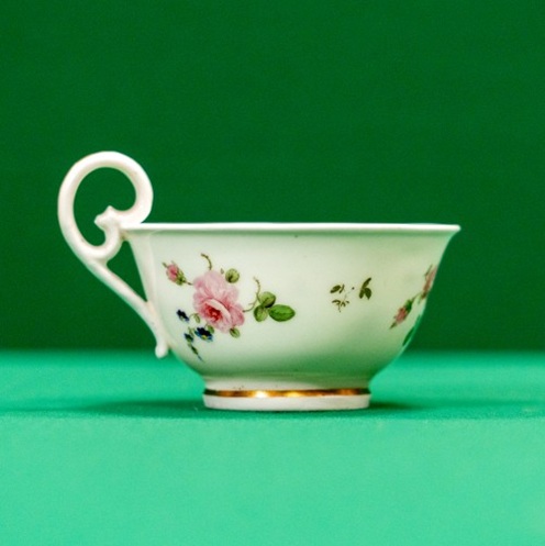 Delicate teacup with curly handle and decoration of roses