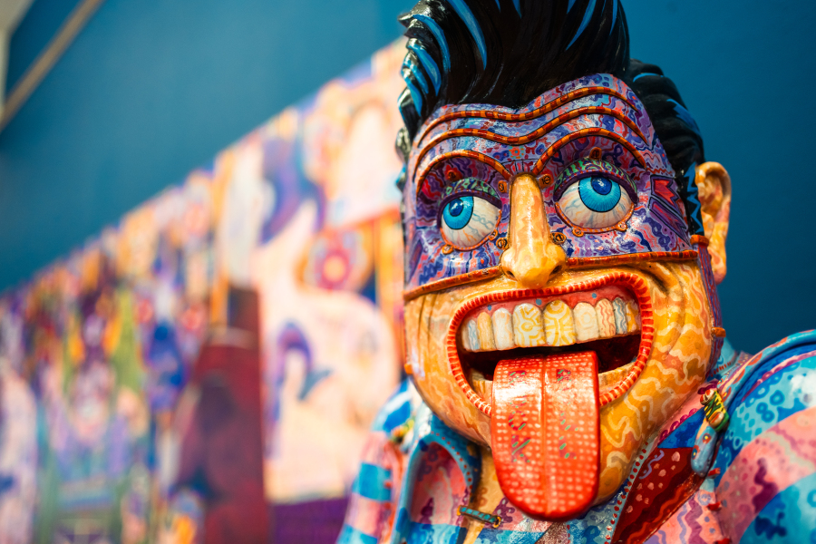 bright coloured comic like sculpture of male with black hair and blue eyes, in superhero costume, with tongue sticking out