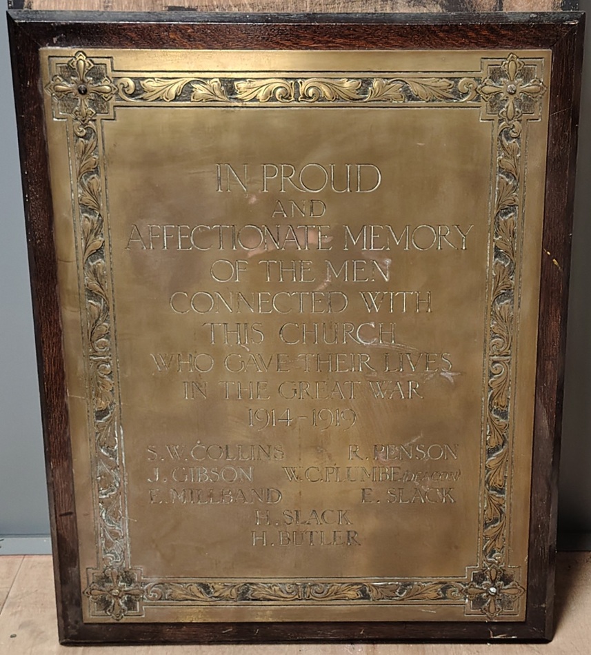 A brass plaque war memorial, mounted on a wooden board