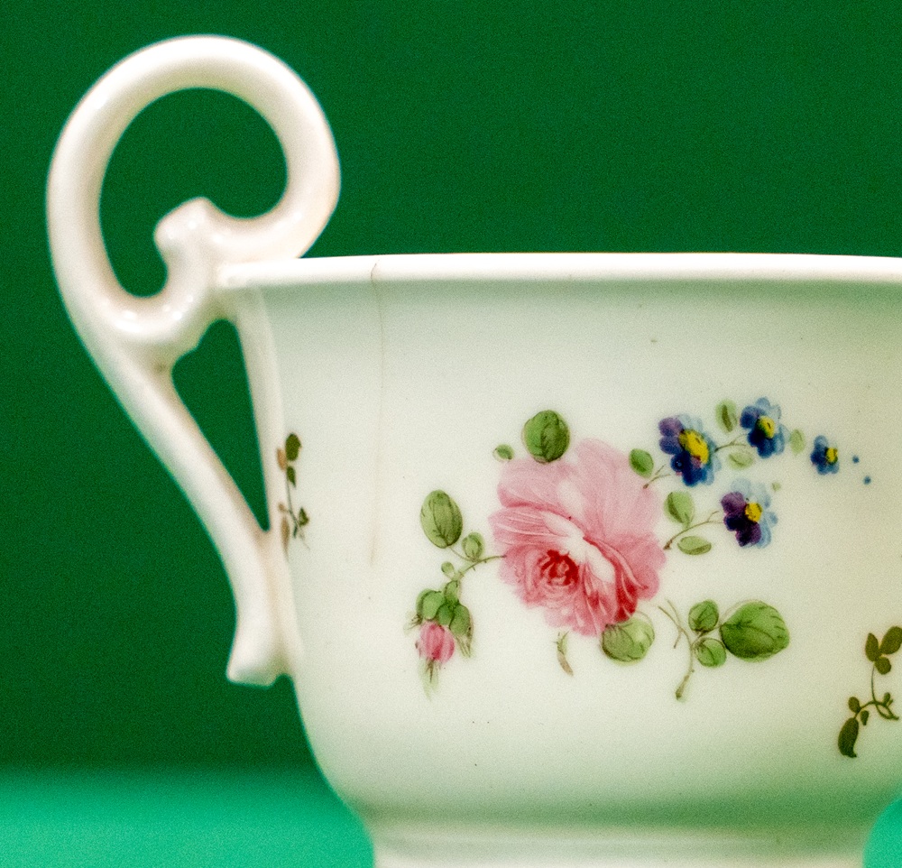 A porcelain coffee cup with an elaborate curly handle and floral decoration