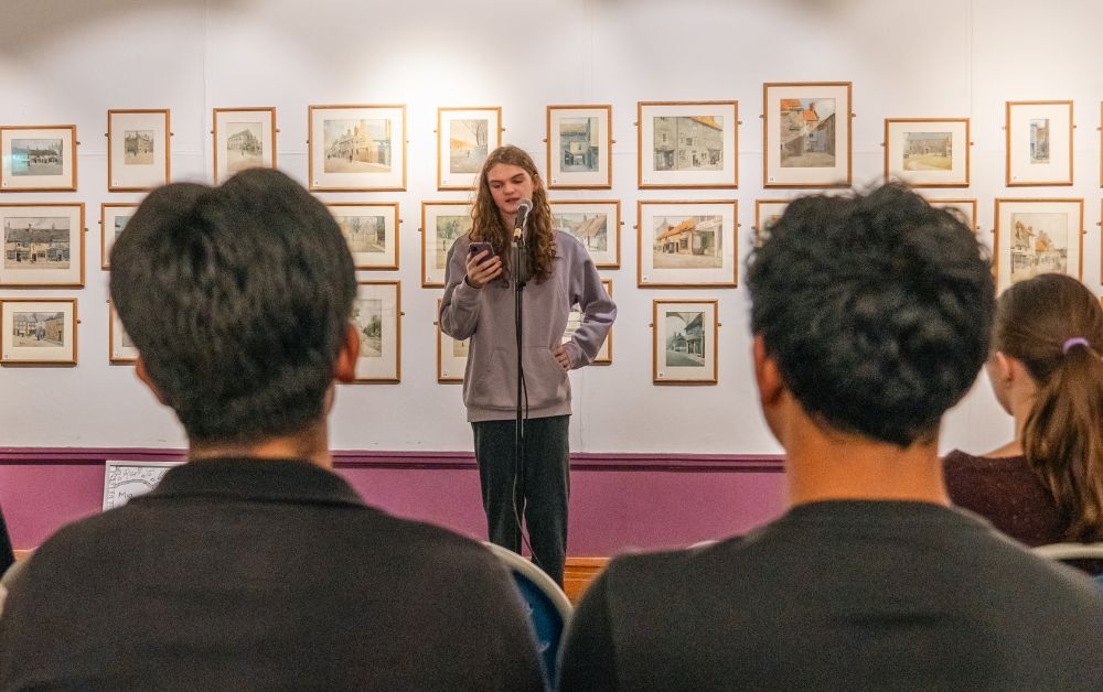 young person standing on stage speaking on a microphone