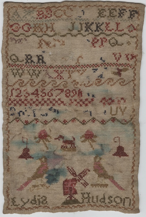 A cross stitch embroidery worked in multi-coloured threads, showing alphabet and digits, and with small pictures of animals, birds, and a windmill