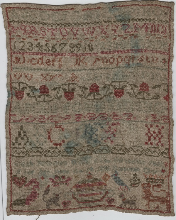 A cross stitch embroidery, worked in multi-coloured thread, showing alphabet and digits, with decorative borders and small pictures of fruit and animals