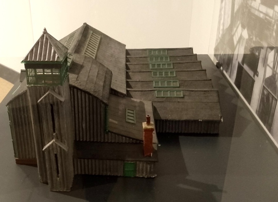 A carboard model of a building with pointed, corrugated iron, roofs