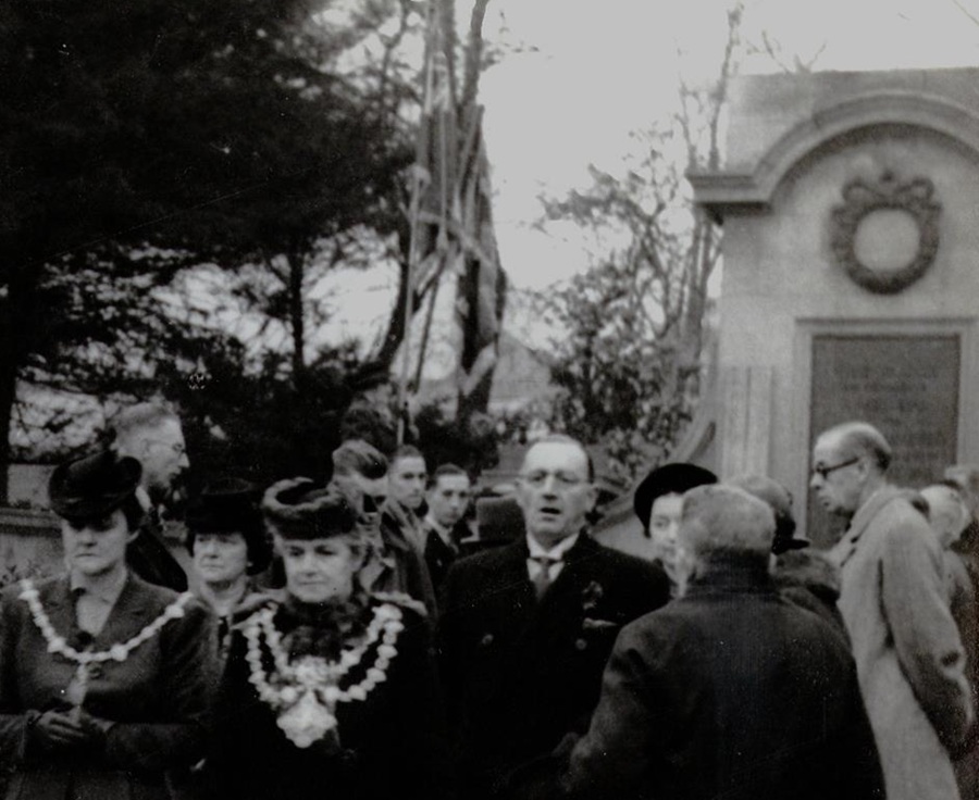 A black and white photograph of a group of dignitaries in front of a memorial
