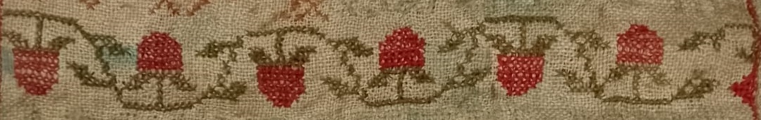 A detail from a cross stitch embroidery, showing a horizontal border of twisting vines and berries