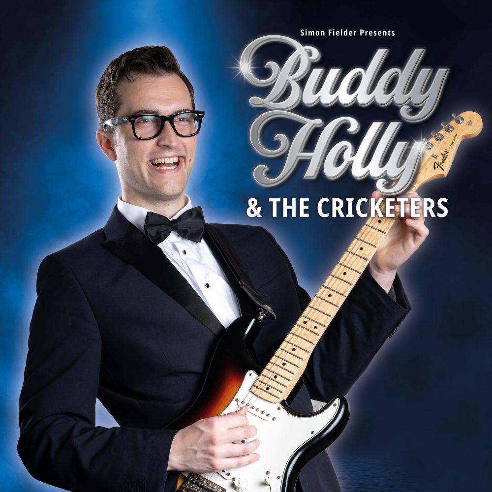 man in glasseswearing smart suit and bow tie smiling holding electric guitar